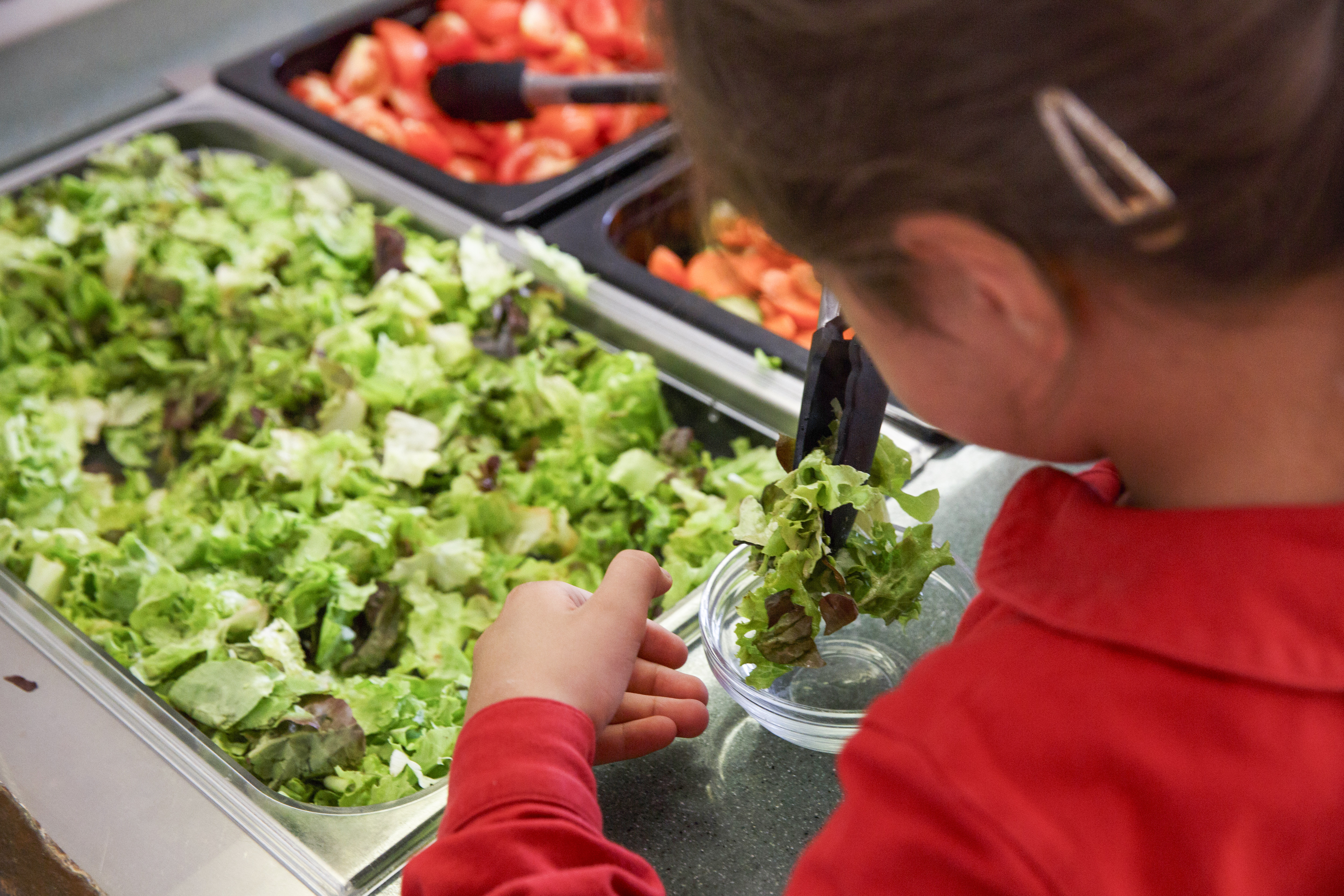 Kind steht an einer Salatbar und stellt sich ihren Salat zusammen in der Kantine der Phorms Grundschule Hamburg