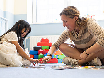 Kind und Erzieherin sitzen auf dem Boden und machen gemeinsam ein Puzzle in der Phorms Kita Hamburg