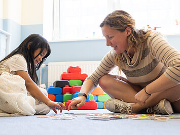 Kind und Erzieherin sitzen auf dem Boden und machen gemeinsam ein Puzzle in der Phorms Kita Hamburg