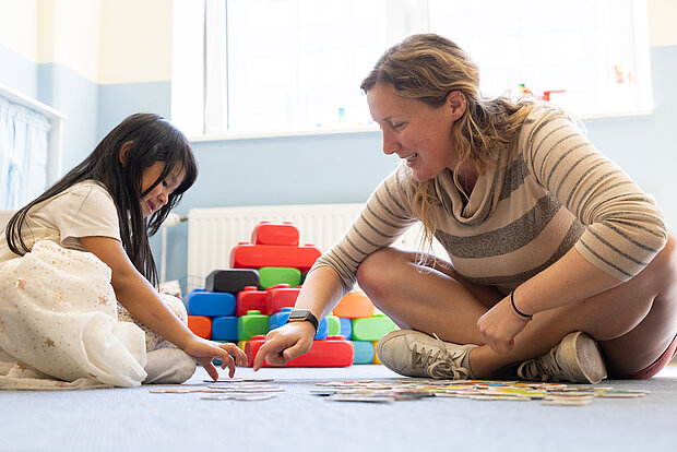 Kind und Erzieherin sitzen auf dem Boden und machen gemeinsam ein Puzzle in der Phorms Kita Hamburg